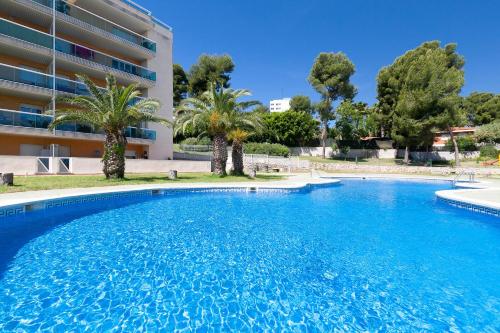 a large swimming pool with palm trees in front of a building at UHC Bellavista Apartments in Salou