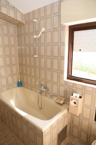 a bath tub in a bathroom with a window at Rooms and Apartments Kurtović in Donji Seget