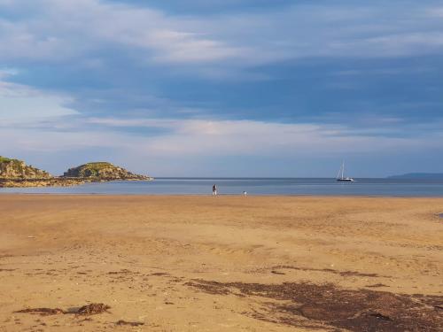 a person walking on a beach with a boat in the water at Drumfearne Guesthouse & Tearoom in Carradale