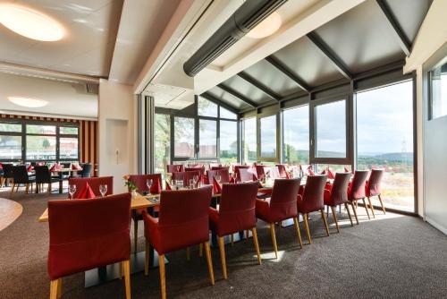 a dining room with red chairs and tables and windows at Hotel & Golfrestaurant Gut Wissmannshof in Staufenberg
