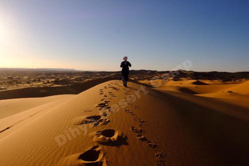 a man walking on a sand dune in the desert at Dihya desert camp in Merzouga