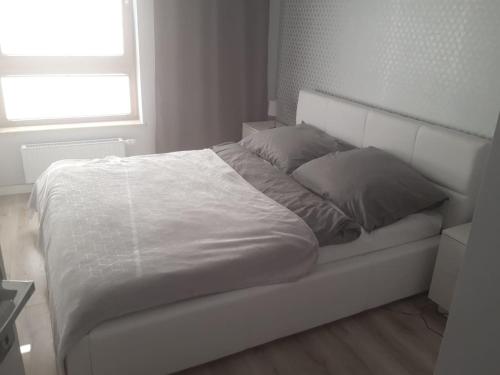 uma cama branca num quarto branco com uma janela em Apartament Nowa Letnica em Gdansk