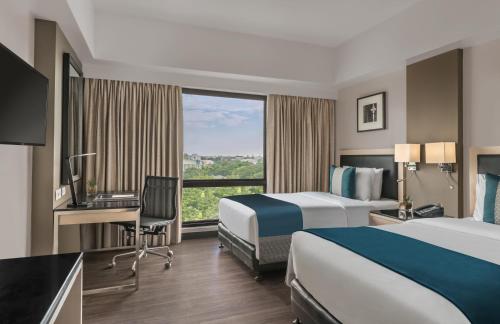 Habitación de hotel con 2 camas, escritorio y ventana en Seda Capitol Central Hotel en Bacolod