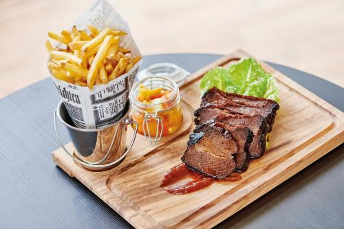 a steak and french fries on a cutting board with a sandwich and a cup thereof at Sorell Hotel Ador in Bern