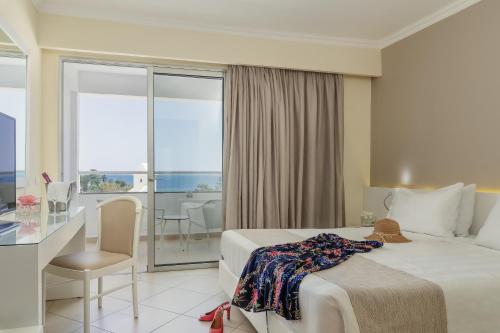 a hotel room with a bed and a desk and a balcony at Lindos Village Resort & Spa - Adults Only in Líndos