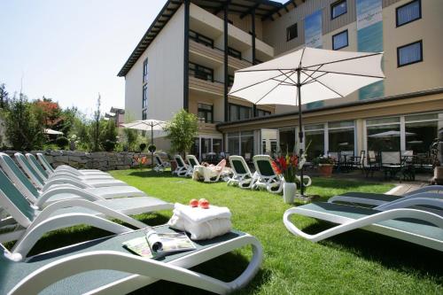 a row of lounge chairs and an umbrella on a lawn at Wunsch Hotel Mürz - Natural Health & Spa Hotel in Bad Füssing