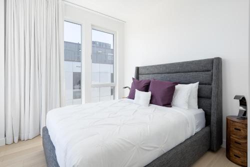 a white bedroom with a large bed with purple pillows at Le Se7t Penthouses in Montréal