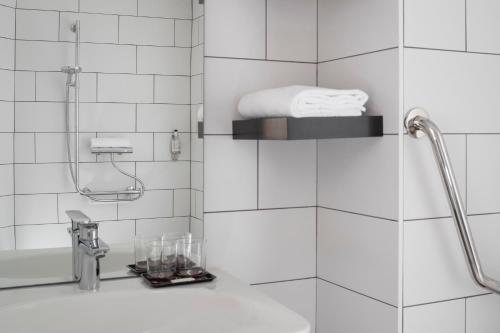 a white tiled bathroom with a shower and a sink at Aka Lodge Lyon Est in Meyzieu