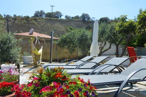 a row of lounge chairs and an umbrella and flowers at Villa Kristi in Loutrá Elevtherón