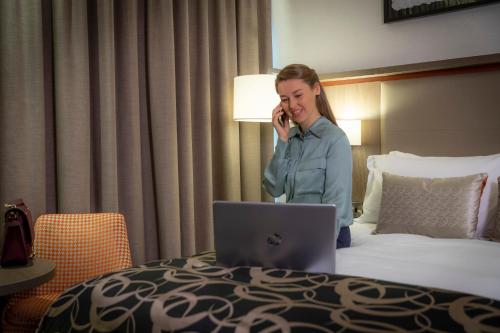 a woman sitting on a bed using a laptop at Clayton Hotel Dublin Airport in Cloghran