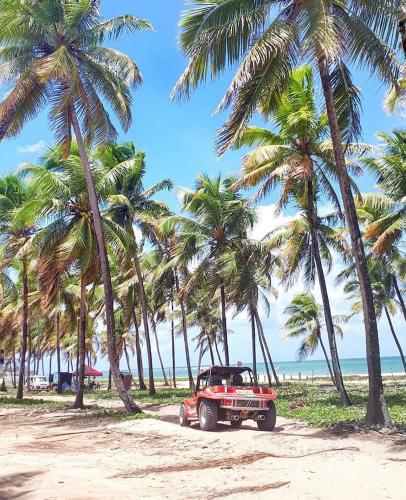 a red truck parked on a beach with palm trees at Pousada Maracabana Spa in Porto De Galinhas