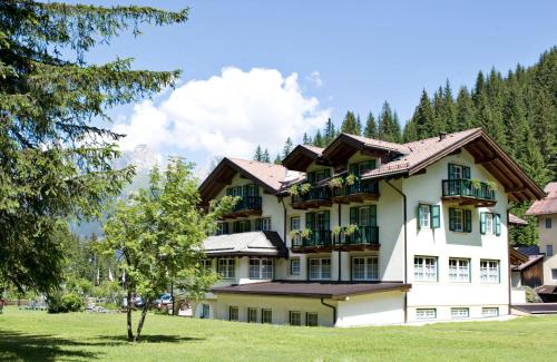 a large white building with balconies and a tree at Hotel Villa Rosella Park & Wellness in Canazei