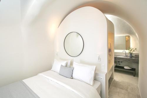 a white room with a bed and a mirror at Aloia Villas in Oia