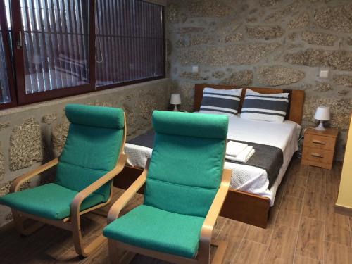 a bedroom with a bed and two green chairs at Casa Campos in Vilarinho