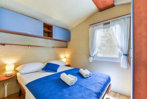 Schlafzimmer mit einem Bett mit blauer Bettwäsche und einem Fenster in der Unterkunft Mobile house 5 Laguna in Turanj