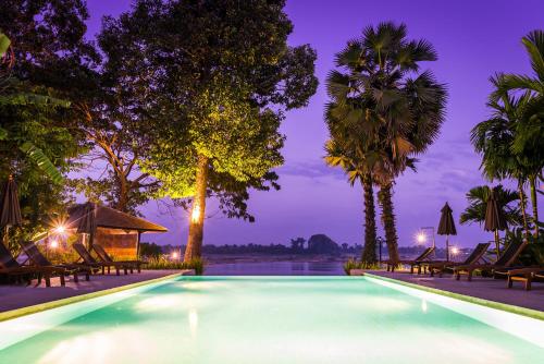チャンパーサックにあるザ　リバーリゾートのヤシの木と椅子が並ぶ夜のプール