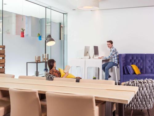 two people sitting on a couch with a man at a piano at Novotel Mechelen Centrum in Mechelen