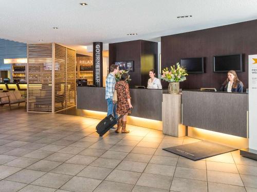 a man and woman waiting at a counter in an airport at Novotel Mechelen Centrum in Mechelen