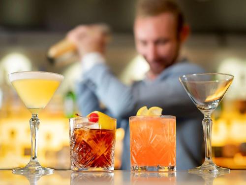 four cocktails on a table with a man in the background at Novotel Sydney International Airport in Sydney