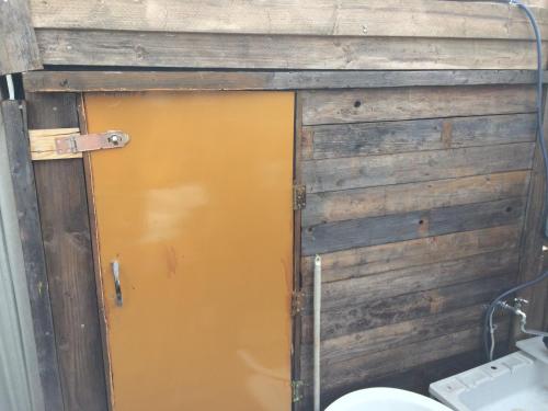 a yellow door in a wooden wall next to a toilet at Tree House & Open Air Bath in Nanae