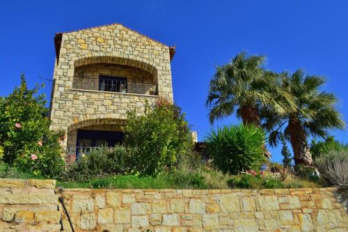 a stone building with a palm tree behind a stone wall at Elouthia Residence with Sea View and Hot Tub in Tsoútsouros