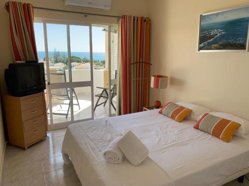a bedroom with a bed and a television and a balcony at Incredible Frontal Sea View - Praia da Galé in Albufeira
