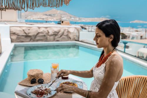 a woman sitting at a table in front of a pool at Bohemian Luxury Boutique Hotel, Adults Only in Naousa