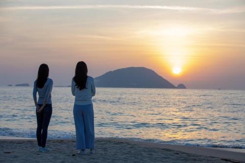 two women standing on the beach watching the sunset at Kyukamura Shikanoshima in Fukuoka