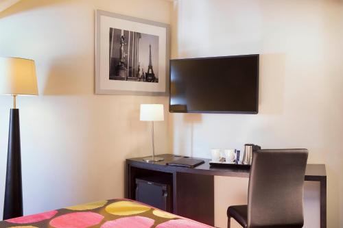 a hotel room with a bed and a desk and a tv at Hôtel Le M in Paris