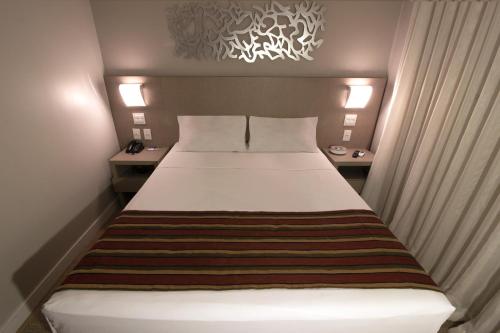 a small bedroom with a bed with a striped blanket at Hotel Beaga Convention Expominas by MHB in Belo Horizonte