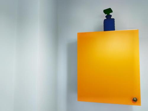 a yellow clipboard on a wall with a blue bottle at Kalokenti Studios in Aegina Town