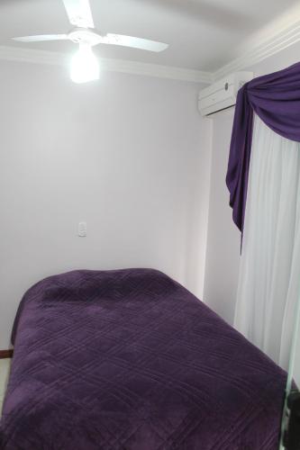 Un dormitorio con una cama morada y un ventilador de techo. en Apartamentos Morada do Sol, en Piratuba