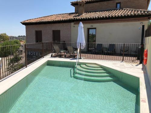 una piscina con sombrilla junto a una casa en Hotel Los Cigarrales en Toledo