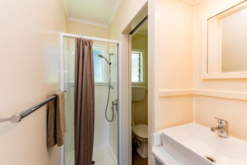 a white bathroom with a shower and a sink at Waitangi Beach Bach 30B in Paihia