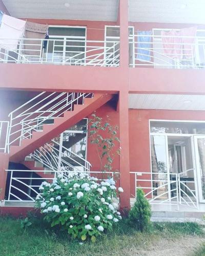 a red building with a staircase and a bush with white flowers at New Wave1 in Grigoleti