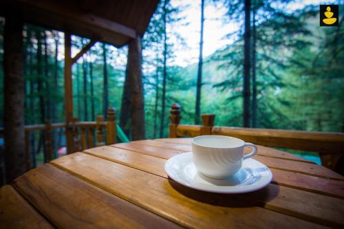 a cup of coffee sitting on a wooden table at LivingStone Ojuven Treehouses in Shimla
