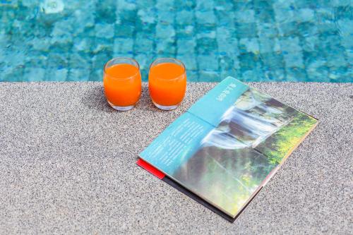 two glasses of orange juice next to a swimming pool at The Seaton House in Rawai Beach