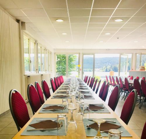 a long table in a room with red chairs at Le Chalet au bord du lac in Gérardmer