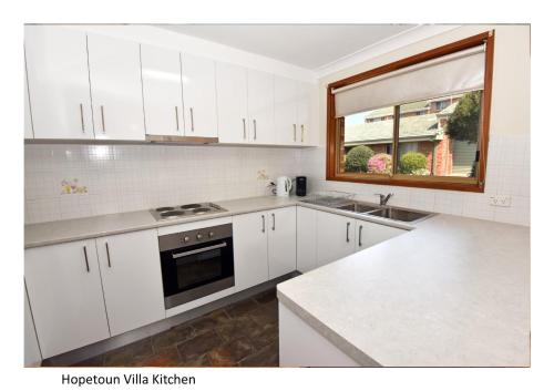 a kitchen with white cabinets and a sink and a window at Hopetoun Villa in Woonona