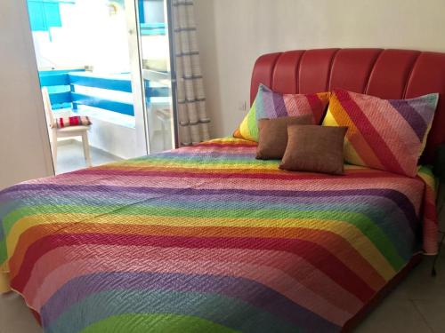 a bed with a rainbow colored blanket and pillows at Complexe Lilia Al jabal in M'diq