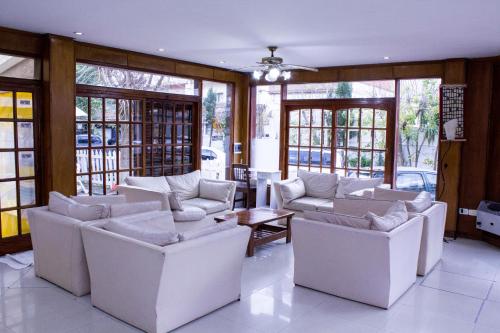 una sala de estar con sofás blancos y mesas y ventanas en el San Remo Palace Hotel de Villa Gesell