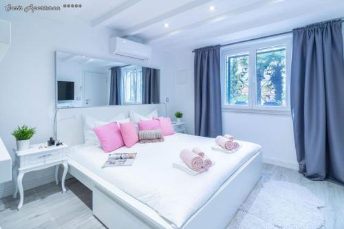 a white bedroom with pink pillows on a bed at Oasis Apartments Opatija in Opatija