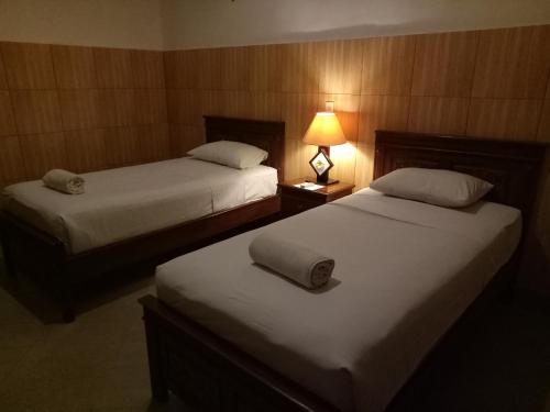 two beds in a hotel room with a lamp on a table at Nitya Home Stay Lembongan in Nusa Lembongan