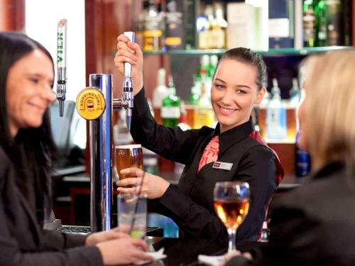 a woman is standing at a bar holding a drink at Mercure Perth Hotel in Perth