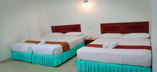 two beds in a room with white walls at Hotel K T Mutiara in Kuala Terengganu
