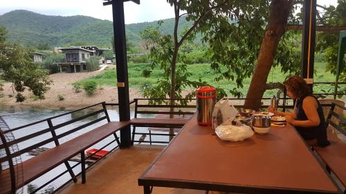 a woman sitting at a table looking out over a river at Kaengkrachan River Hut in Kaeng Krachan
