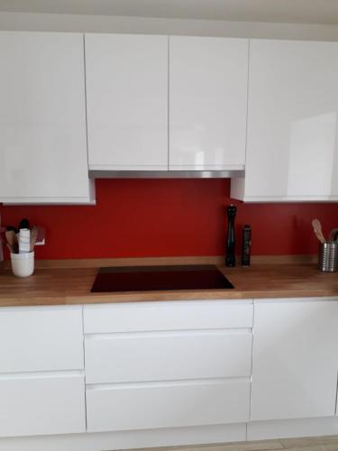 a kitchen with white cabinets and a red wall at Gîte des Ayrifagnes in Theux