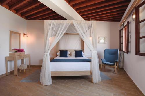 a bedroom with a canopy bed and a blue chair at Thea Villas and Suite in Líndos