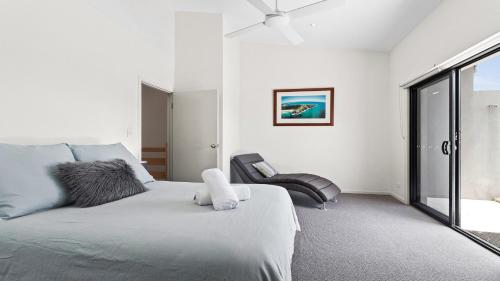 a white bedroom with a bed and a chair at Aqua on Fletcher Street in Byron Bay