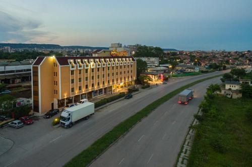 a large building on a street with cars and trucks at Adamo Hotel in Varna City